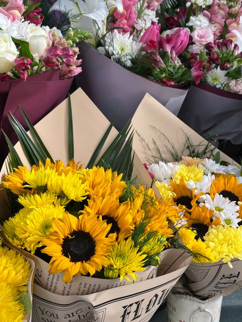 An assortment of freshly arranged flower bouquets displayed together, featuring a vibrant mix of yellow sunflowers with large dark centers, white daisies with yellow centers, and pink and white tulips